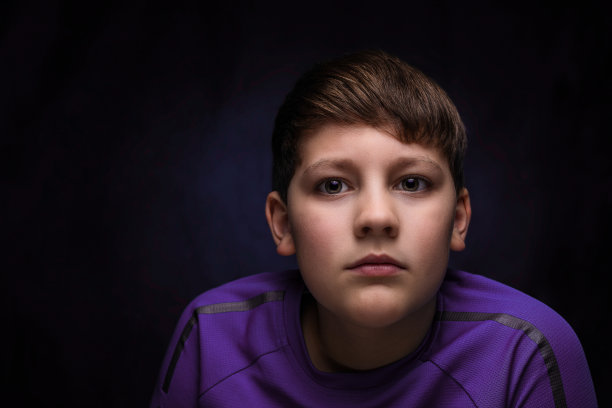 一个英俊的十几岁男孩的肖像与暗金色头发和刘海穿着一件运动紫色t恤在一个孤立的背景图片下载