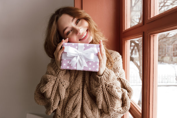 照片满意的年轻女子20岁与棕色头发看在相机上，并持有生日礼物盒室内图片下载