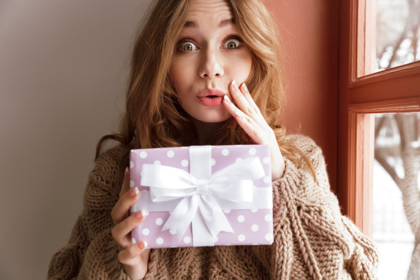 有魅力的年轻女子20岁的照片与棕色头发看在相机上，并拿着生日礼盒室内图片下载