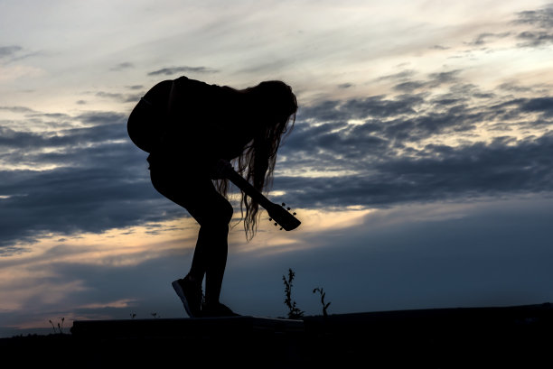 在落日的背景下，一个拿着吉他的女人的剪影图片下载
