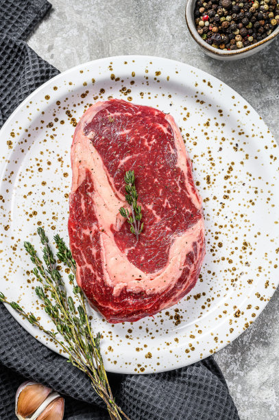 生鲜肉肋眼牛排加调味后放在砧板上。肋眼牛排。灰色的背景。俯视图图片下载