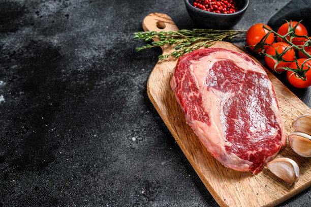 生鲜肉肋眼牛排加调味后放在砧板上。肋眼牛排。黑色背景。前视图。本空间图片下载