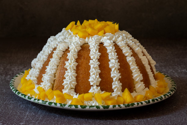 Zuccotto芒果。传统的意大利蛋糕放在白色和绿色的盘子上，上面装饰有奶油和芒果，背景是灰色的。图片下载