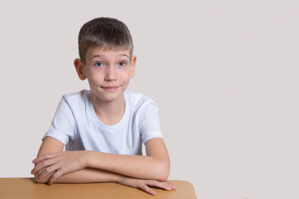 英俊的聪明微笑的男孩坐在桌子上，期待在一个灯光背景，拷贝空间图片下载