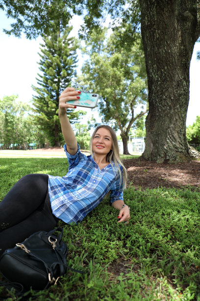 美丽年轻的成年女子与手机在绿色的草地上图片下载