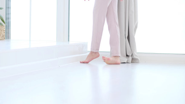 侧面近距离观看无法辨认的女人脚腿，赤脚的女孩站在室内的现代家庭享受温暖的木地板。软焦点图片下载