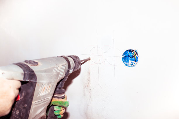 一个工人用钻头钻墙。房间里有额外的电源插座。修理和改善房屋图片下载