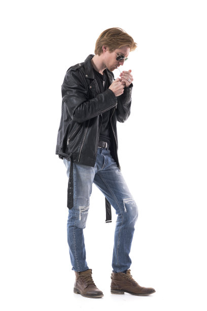 侧面的年轻时尚摇滚或摩托车男点燃香烟覆盖与手。图片下载