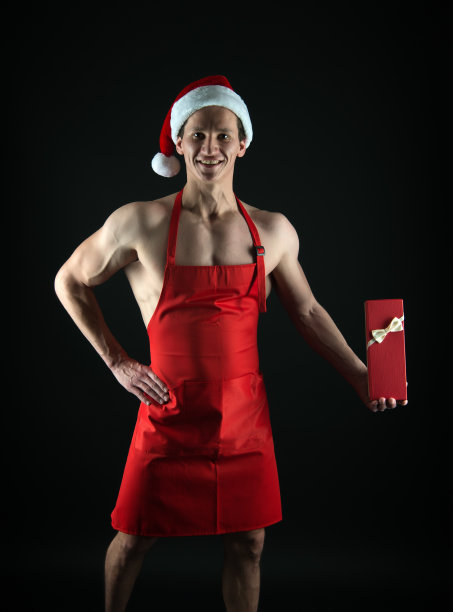 圣诞节的配方。圣诞精神。圣诞节的传统。圣诞快乐。肌肉男戴着圣诞老人的帽子。黑色背景上的健美运动员。冬天的假期。肌肉发达的运动员庆祝新年图片下载