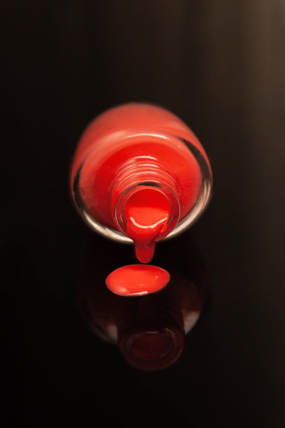 一个红色指甲油瓶子的侧面，在黑色的背景下反射在镜面上图片下载