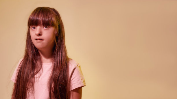 残疾女孩的肖像与唐氏综合症看着一边，而摆出孤立在创造性的黄色背景图片下载