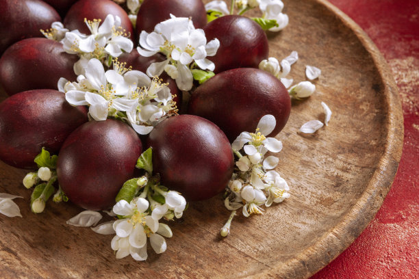 这是一张特写照片，红色的传统复活节彩蛋放在一个古老的木制盘子上，红色的背景是苹果花。俯视图，复制空间图片下载