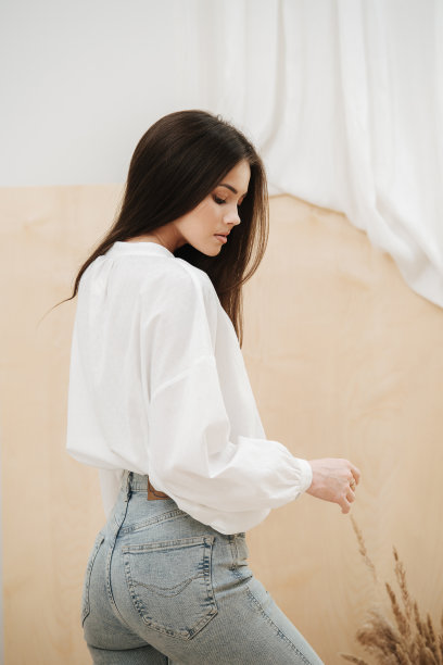 性感美丽的女人穿着紧身牛仔裤和白衬衫。从侧面看。图片下载