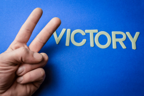 人的手做一个胜利标志旁边写着塑料字母在蓝色的纸背景，概念图片下载