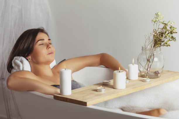 年轻漂亮的女人在一个明亮的浴室内的烛光下用泡沫洗澡，放松图片下载