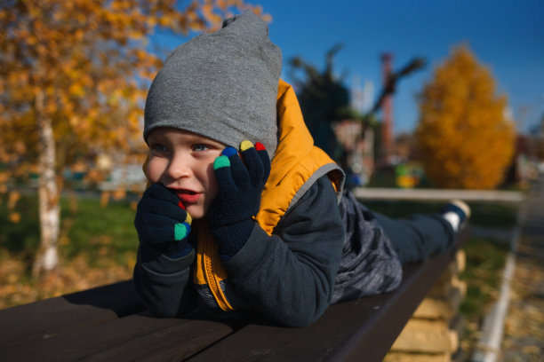 一个孩子在秋天的公园里独自忧伤。一个白种人模样的小男孩躺在长凳上。图片下载