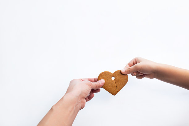 妈妈和宝宝的手拿着半块心形的姜饼。情人节的概念图片下载