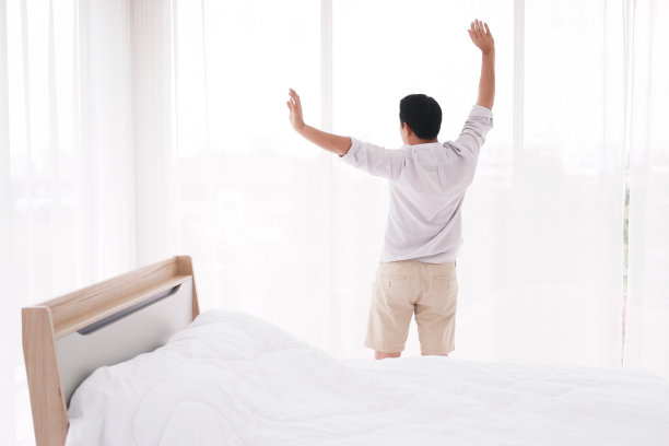 一名亚洲男子在卧室醒来后正在懒洋洋地伸懒腰。小睡之后他觉得神清气爽。图片下载