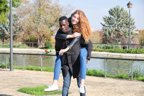 非洲黑人男子和红发白人妇女享受骑在背上的玫瑰。年轻的多种族情侣庆祝情人节。图片下载