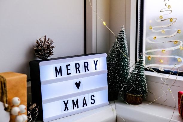 窗台上写着“圣诞快乐”的灯箱。新年装饰品，花环灯和圣诞树。窗户上喷着雪花图片下载