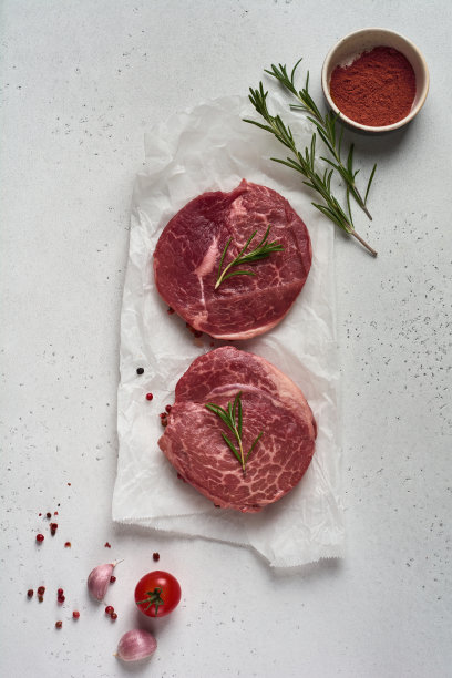 两块新鲜的巴黎生牛排放在白色的羊皮纸上，加上盐、胡椒和迷迭香，在古老的木制背景上以一种乡村风格呈现。黑安格斯。前视图。图片下载