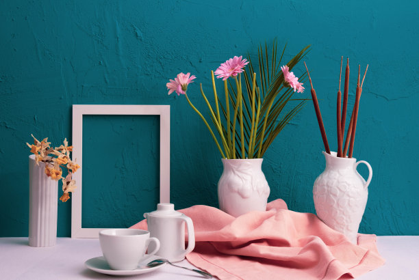 非洲菊，白色相框的照片，一个杯子，咖啡和茶壶和两个花瓶与棉花在蓝色的背景在桌子上图片下载