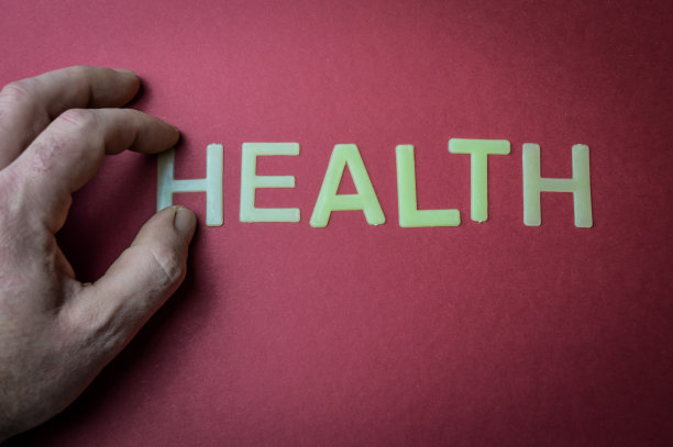 人的手指拿着健康字，用塑料字母写在暗红色的纸背景上，概念图片下载