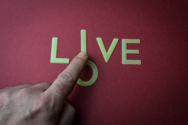 人类手指滑动一个字母到“Love to make it Live”，这是一个用塑料字母写在暗红色纸上的概念图片下载