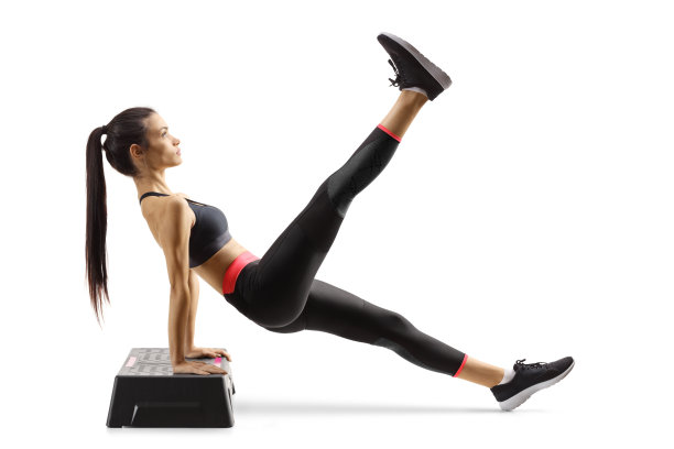 年轻女子在踏步有氧平台上锻炼，抬起一条腿图片下载