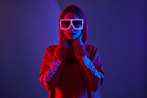 时尚年轻女子模特穿帽衫和眼镜太阳镜在霓虹灯工作室的背景。图片下载