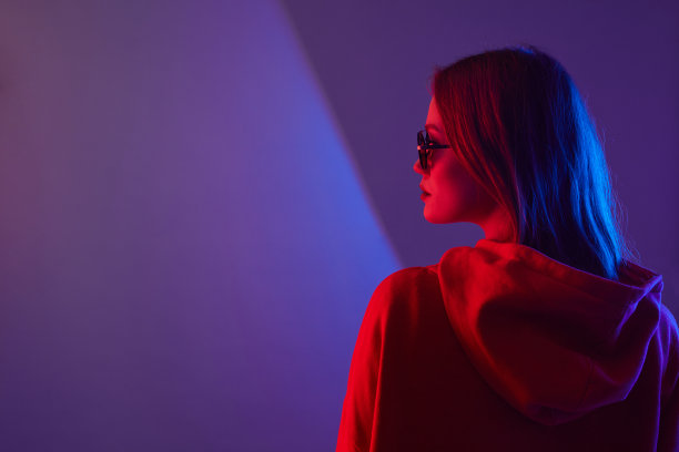 时尚年轻女子模特穿帽衫和眼镜太阳镜在霓虹灯工作室的背景。图片下载