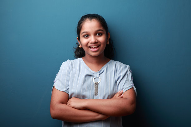 在蓝色的墙壁背景下，一个兴奋的微笑的年轻女孩图片下载