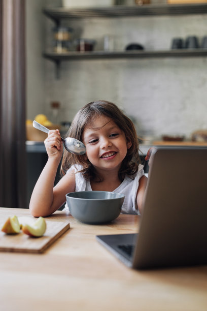快乐的年轻女孩早餐吃麦片，在餐厅用笔记本电脑图片下载