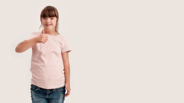 一个患有唐氏综合症的残疾女孩对着镜头微笑，一只手竖起大拇指，孤立地站在白色背景上图片下载