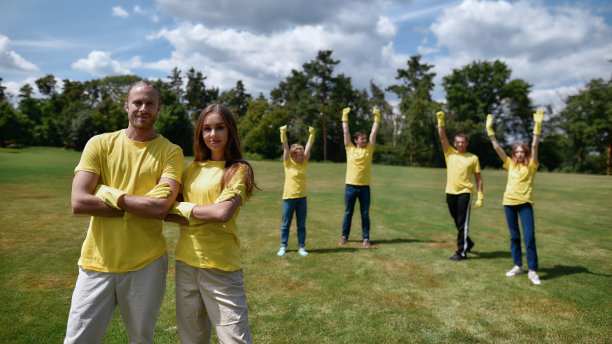保存自然。一群年轻人，快乐的志愿者穿着制服，戴着橡胶手套，在公园清理垃圾时对着镜头微笑图片下载