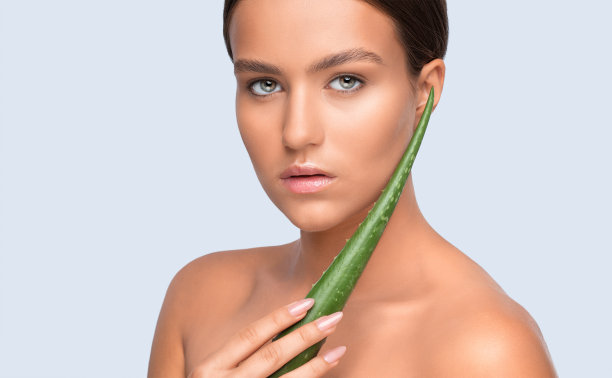 一个美丽的女人的肖像与绿色芦荟叶，裸露的肩膀，健康清洁的皮肤和新鲜的化妆。美学美容和化妆概念。图片下载