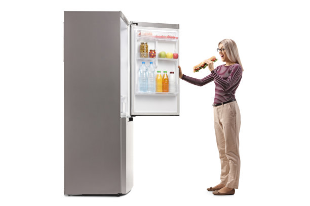 一个快乐的年轻女人拿着三明治站在冰箱前，还拿着门图片下载