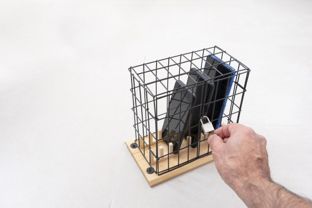 用手打开或关闭一个笼子上的锁，用一个挂锁锁在笼子里的三部手机，社会隔离或手机滥用和社交网络的概念，白色背景，水平图片下载