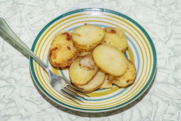 用叉子把薄皮的热烤土豆片放在盘子里。这是上班族和单身人士下班后简单快捷的一餐。穷人和农民的廉价食物图片下载