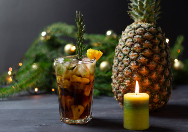 圣诞和新年鸡尾酒菠萝，朗姆酒，可乐，冰，薄荷，迷迭香玻璃在黑色的木头背景燃烧蜡烛，新鲜的水果，装饰冷杉树枝图片下载