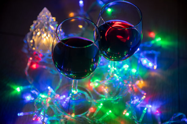两个玻璃杯在一个明亮的圣诞树的背景和一个多色的花环在黑暗的背景。新年的庆祝活动。图片下载