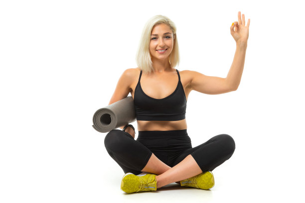 一个年轻的运动女孩，金发和明亮的指甲，穿着黑色运动上衣，打底裤和黄色运动鞋拿着一个运动垫。图片下载