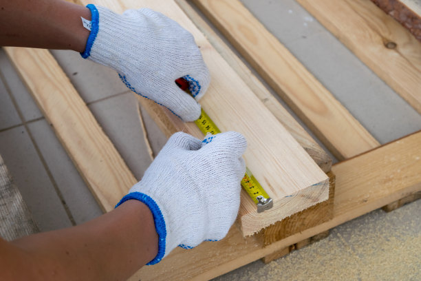 一个戴着白色施工手套的男人用卷尺量松木板图片下载