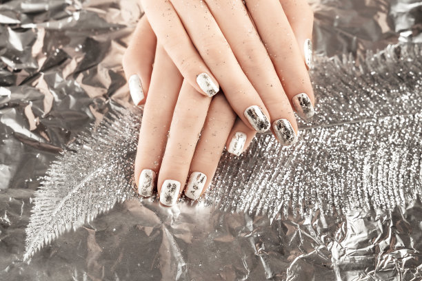 女性手用时髦的银指甲设计在箔背景上握住圣诞装饰金属羽毛。节日背景假日。图片下载