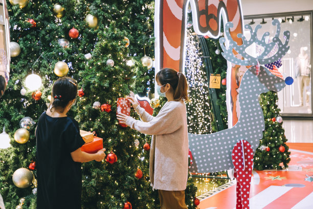 两个亚洲妇女戴着防护面具装饰圣诞树在商场库存照片图片下载