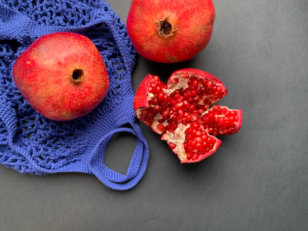 红色，成熟的石榴果实是红色的在一个黑暗的背景与明亮的蓝色绳袋。切成一簇簇成熟的石榴。从上面的照片。石榴果实的季节。水果成熟图片下载