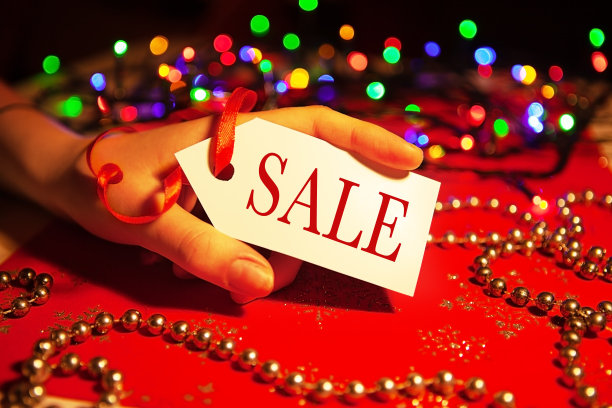 在圣诞节和新年假期期间，一名妇女的手拿着一个白色标签，上面写着“销售”，这是装饰过的圣诞背景。图片下载