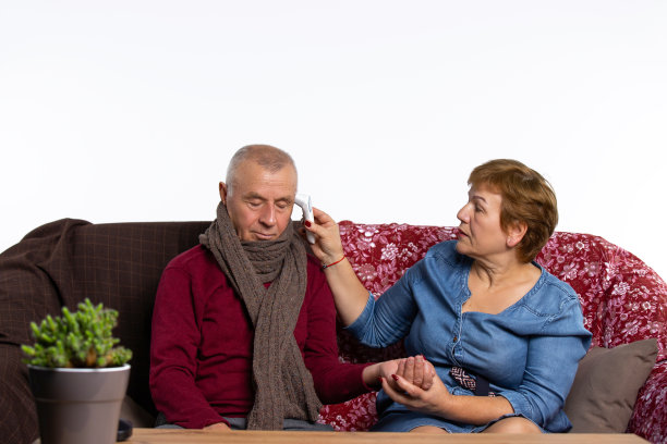 老年妇女用体温计给生病的丈夫测量发烧。在家里与病毒感染作斗争。图片下载