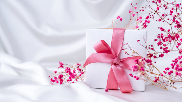 白色礼盒，以白色丝织物为背景，配以粉色丝带和粉红色小花。节日贺卡图片下载