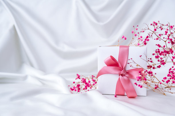 白色礼盒，以白色丝织物为背景，配以粉色丝带和粉红色小花。节日贺卡图片下载